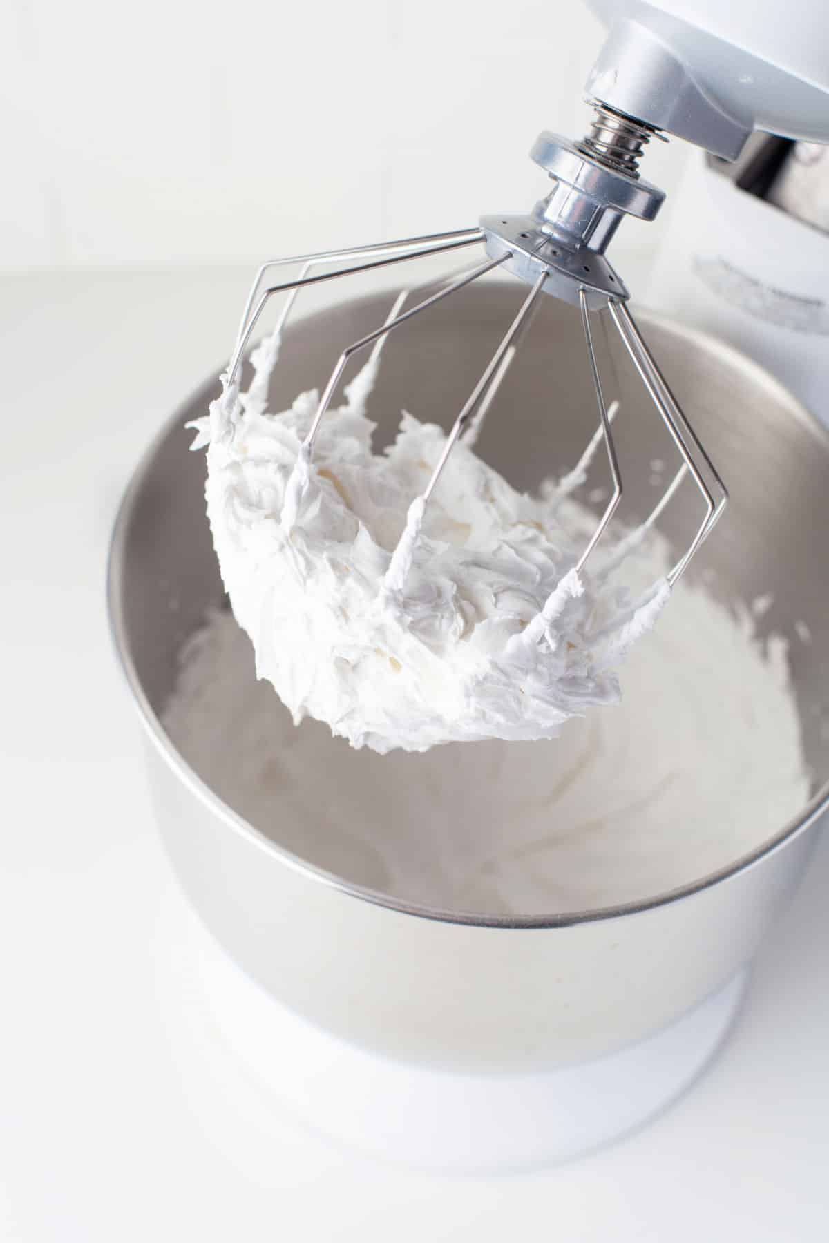 A stand mixer whisk with beaten royal icing on it. 
