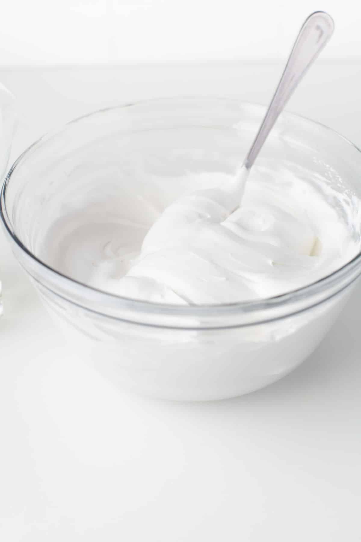 A glass mixing bowl full of royal icing with a silver spoon in it. 