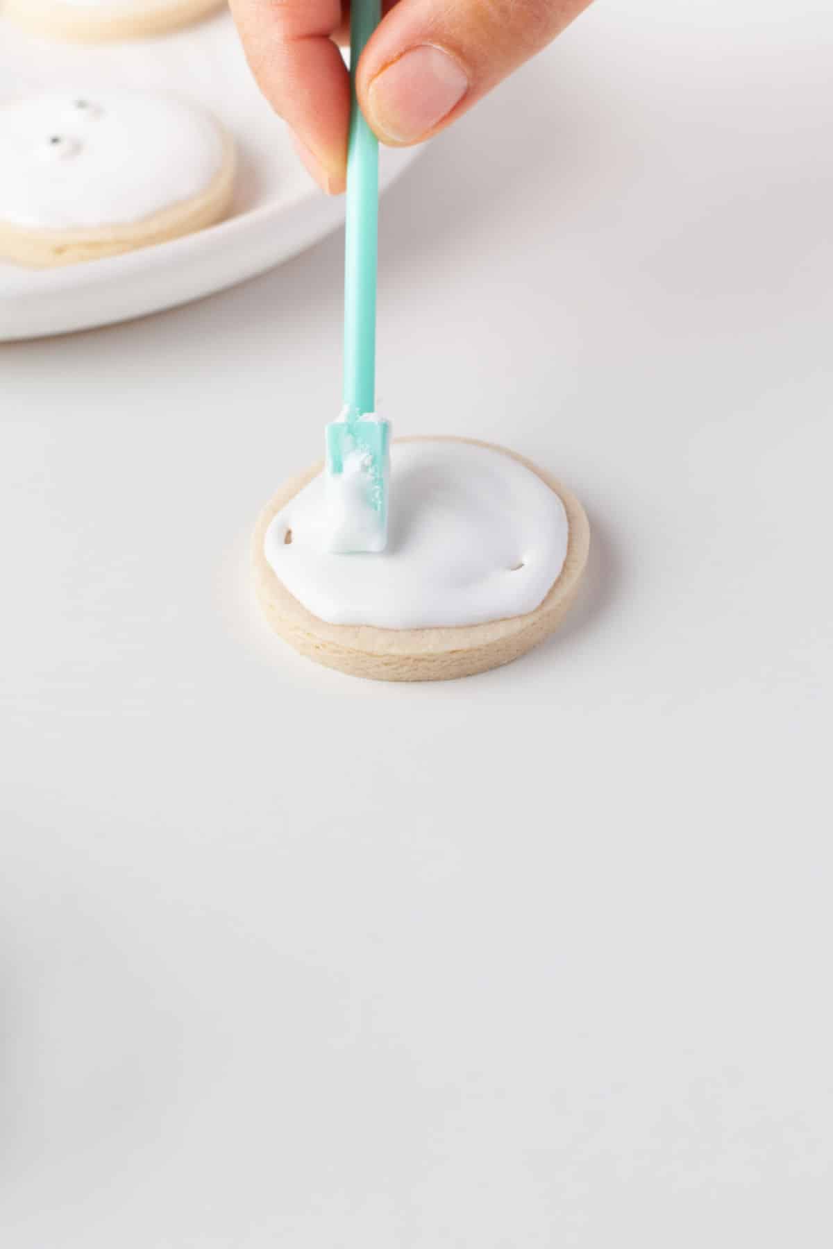A teal tool smoothing out royal icing on a cookie. 