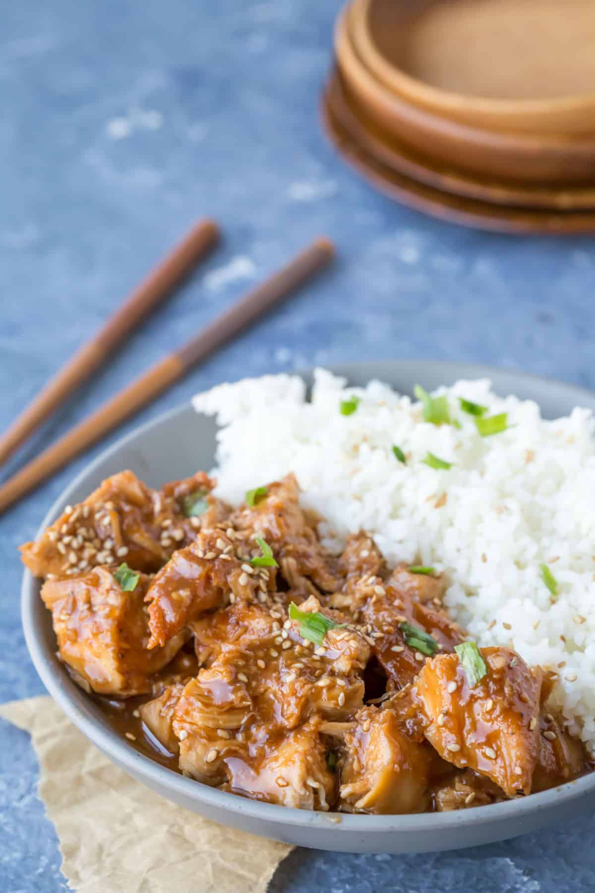 A dish of crock pot sesame chicken topped with sesame seeds and green onions. 