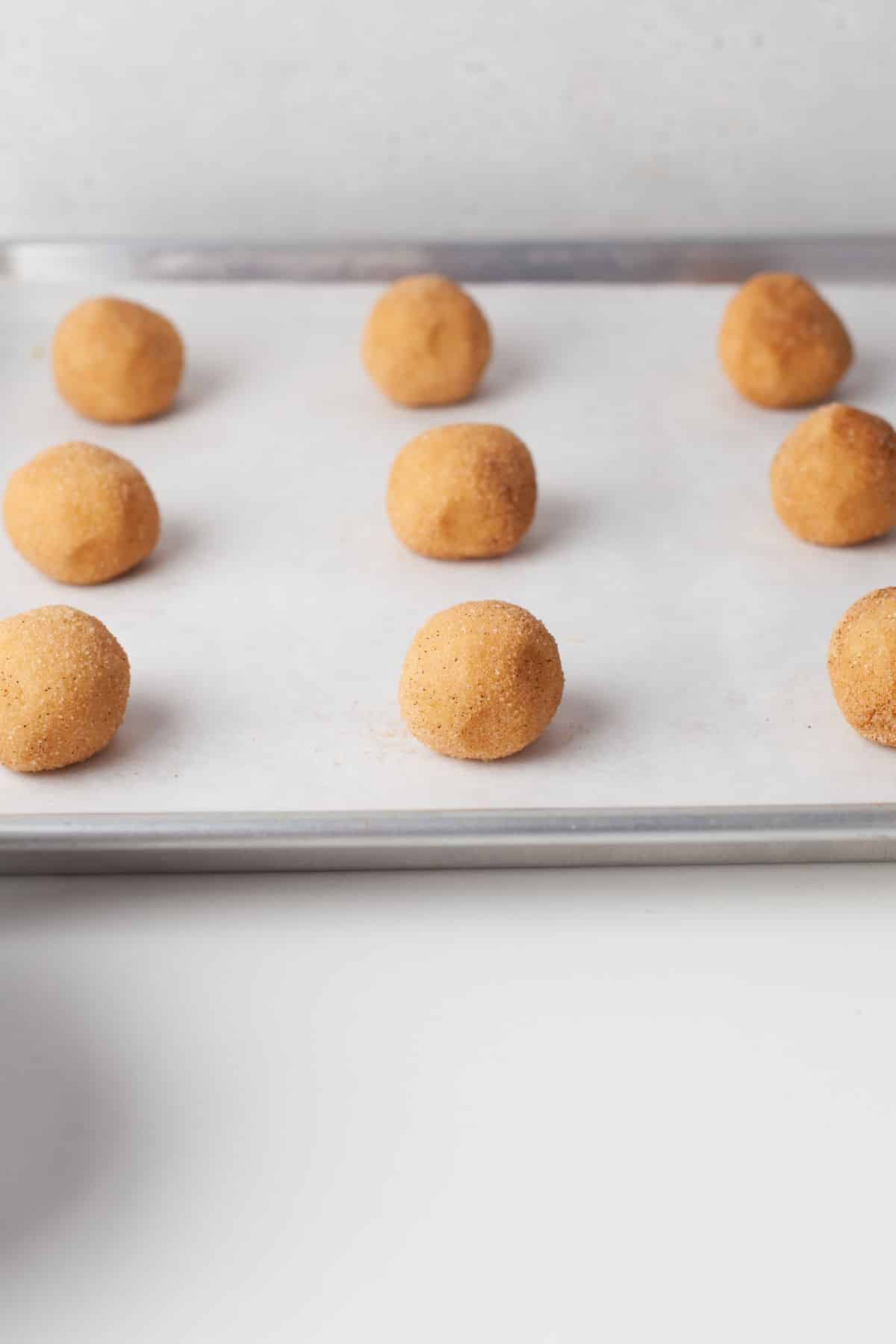 Scoops of cookie dough on a parchment lined baking sheet. 