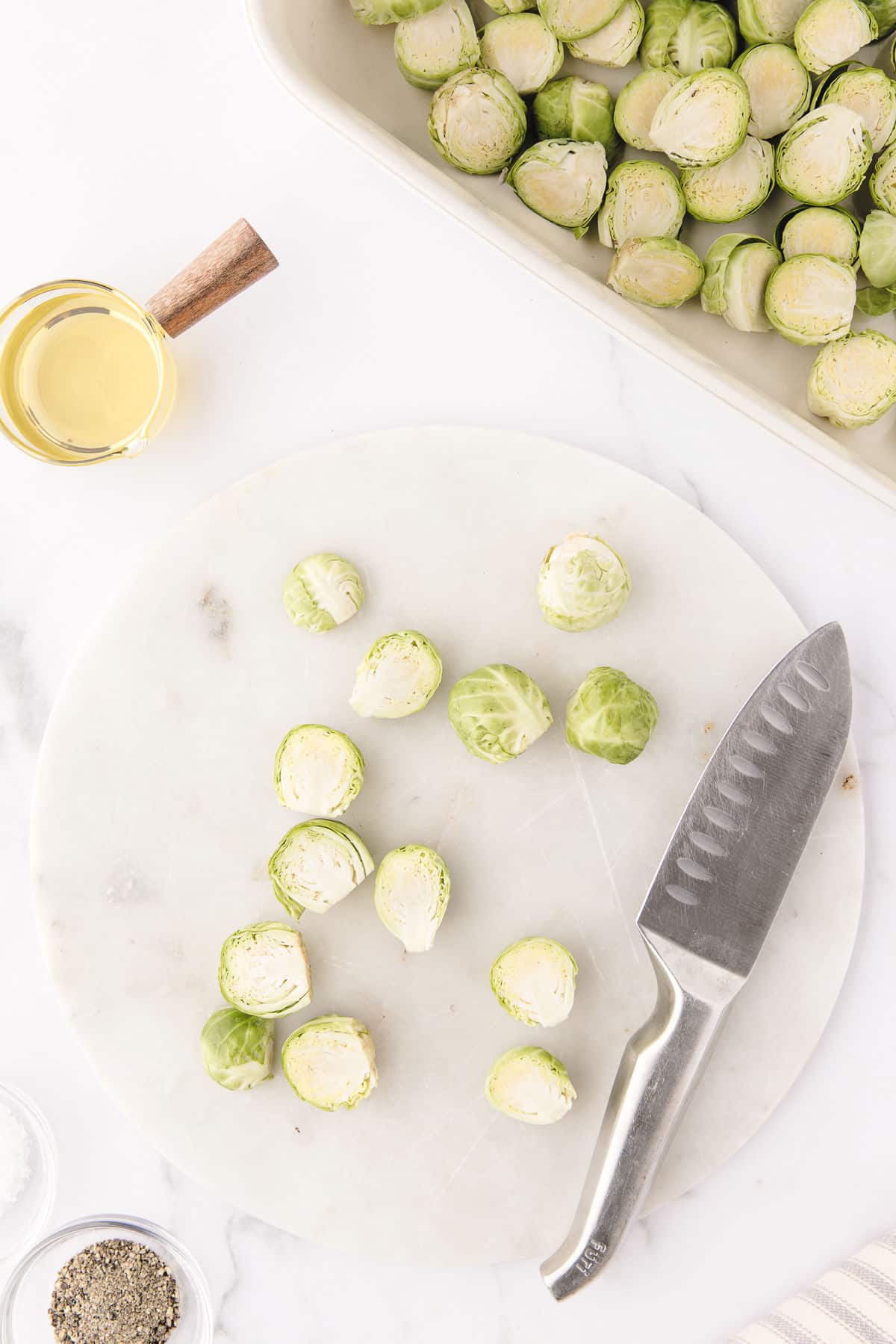 A knife and a few Brussels sprouts cut in half on a white cutting board. 