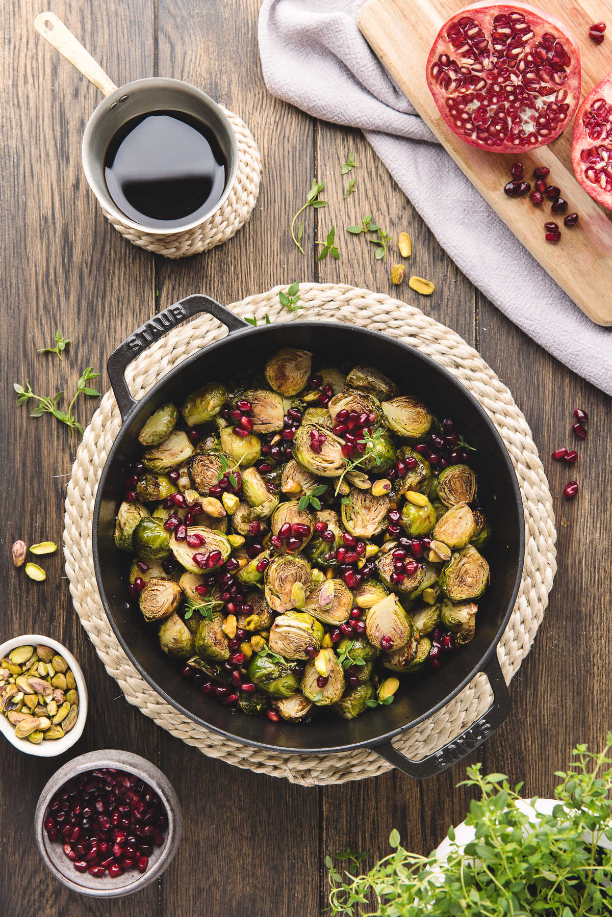 A dish of Brussels sprouts next to a cup of balsamic glaze and half of a pomegranate. 