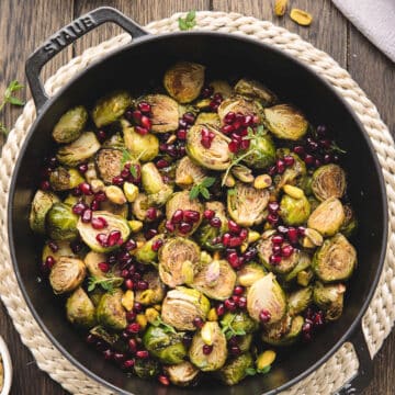 A cast iron dish of roasted Brussels sprouts with balsamic glaze on a jute placemat.