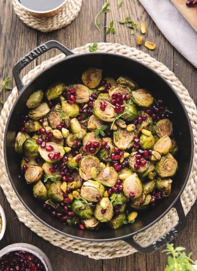 A cast iron dish of roasted Brussels sprouts with balsamic glaze on a jute placemat.