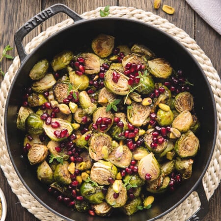 A cast iron dish of roasted Brussels sprouts with balsamic glaze on a jute placemat.