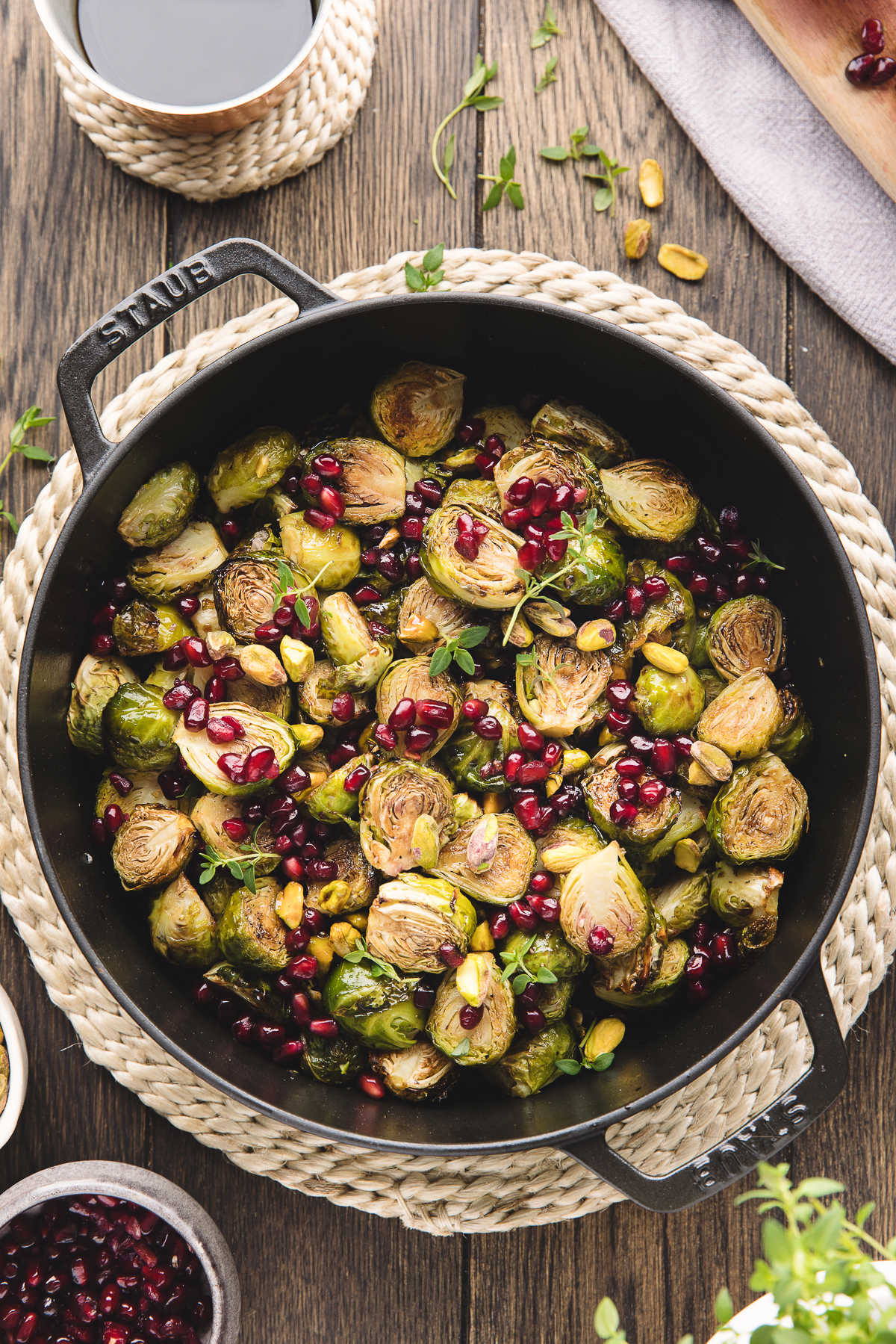 A cast iron dish of roasted Brussels sprouts with balsamic glaze on a jute placemat. 