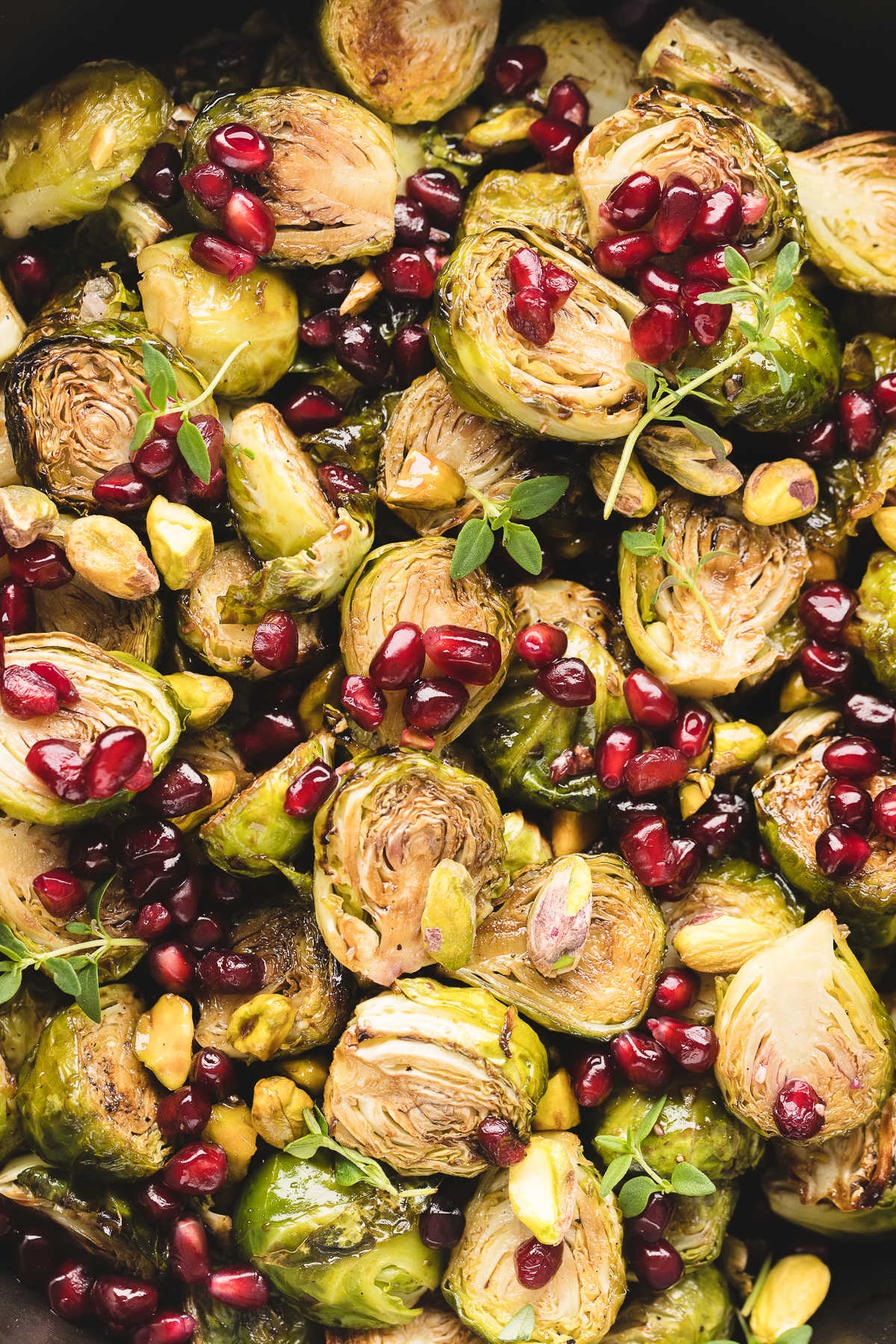 Close up photo of roasted Brussels sprouts topped with pomegranate seeds and chopped pistachios. 