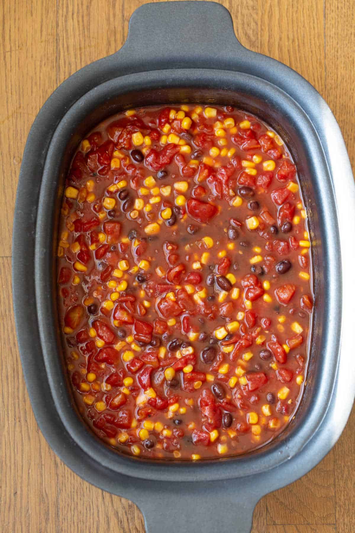 Corn tomatoes beans and sauce in a slow cooker insert. 