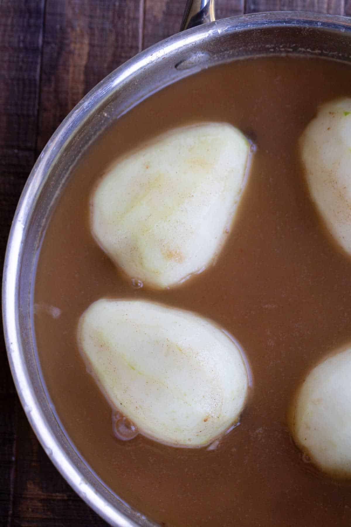 Pear halves in cider in a saucepan. 