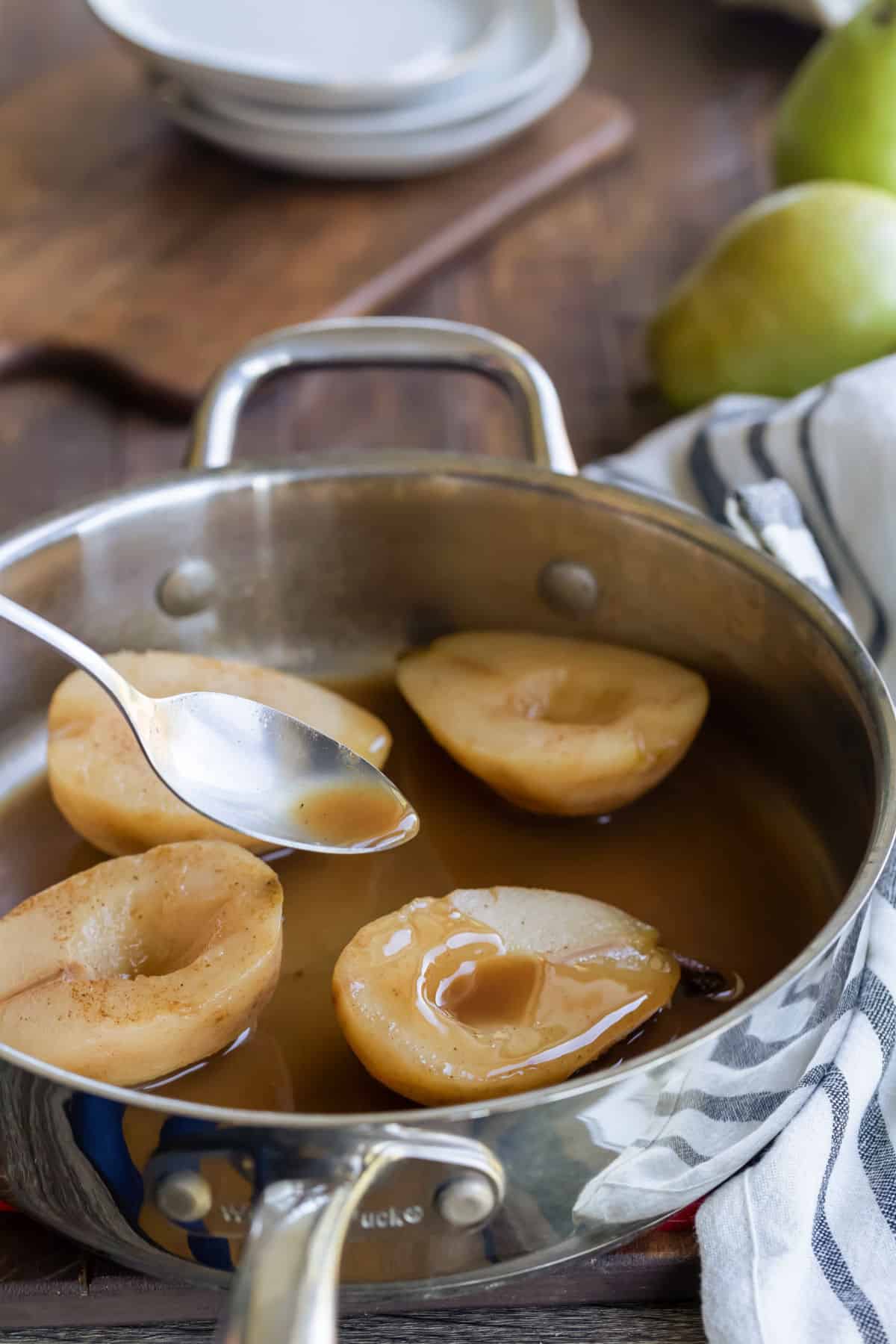 Silver spoon pouring cider sauce onto cider poached pear.