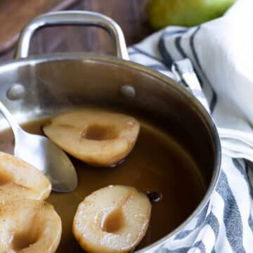 Poached pears in cider in a saucepan.