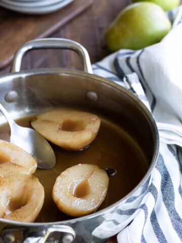 Poached pears in cider in a saucepan.