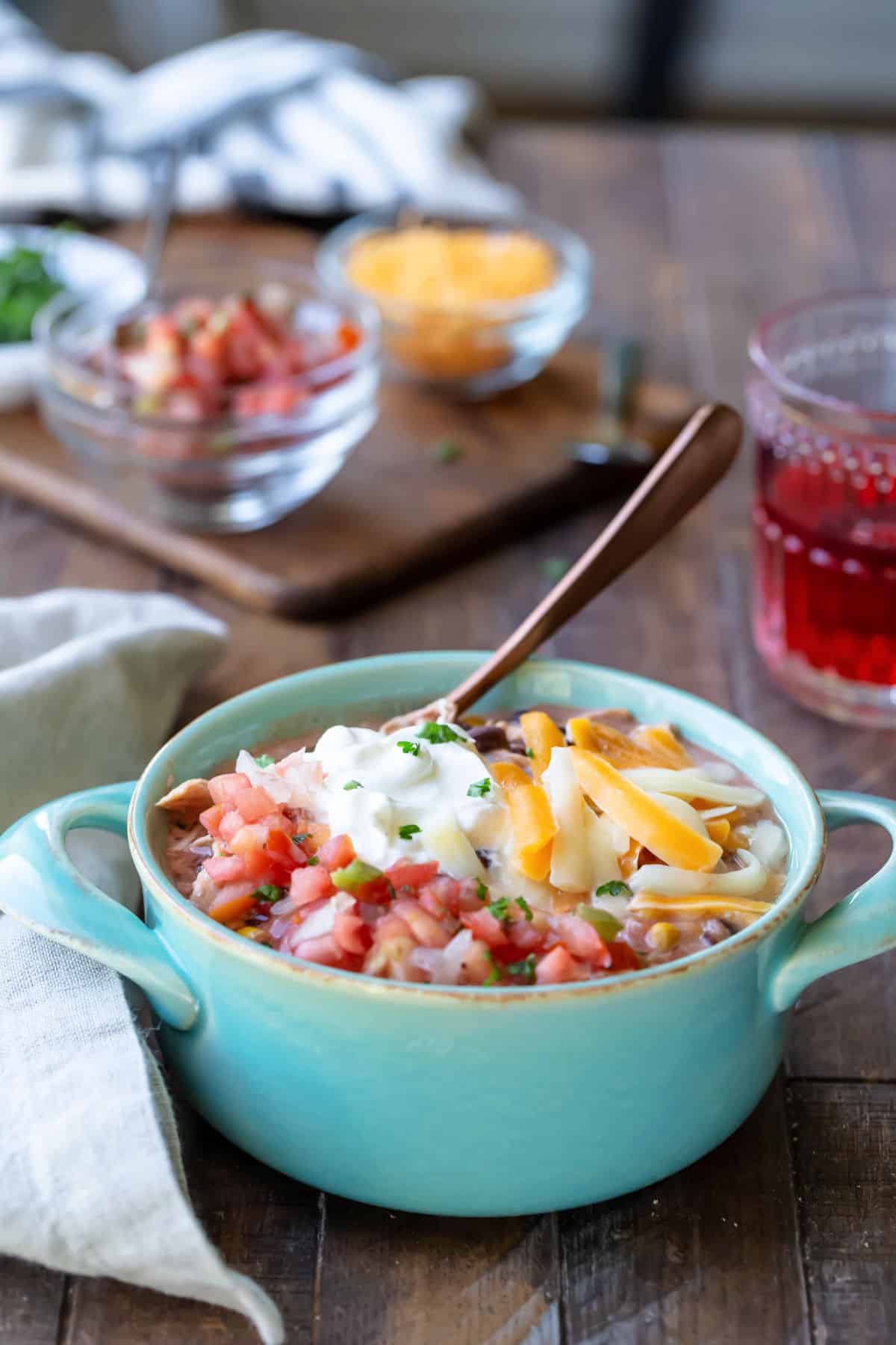 A crock pot chicken enchilada chili next to dishes of cheese and pico de gallo. 