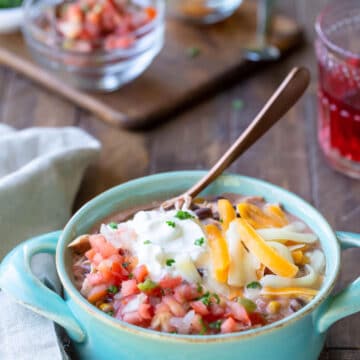 Slow cooker chicken enchilada chili in an aqua crock with a copper spoon in it.