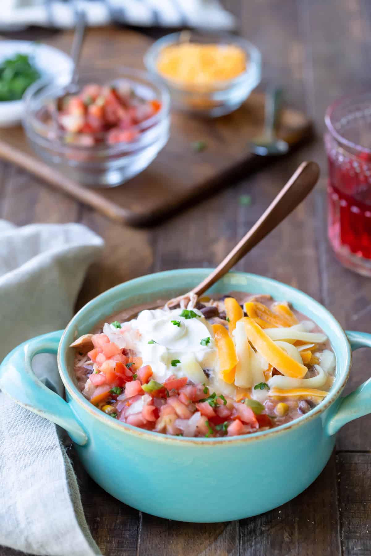 Slow cooker chicken enchilada chili in an aqua crock with a copper spoon in it.