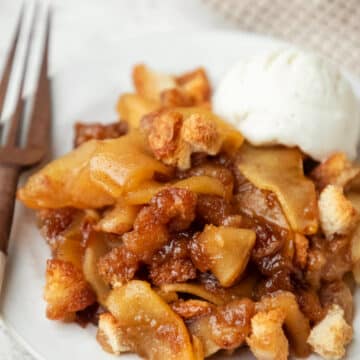 A white plate with apple brown betty and a scoop of vanilla ice cream.