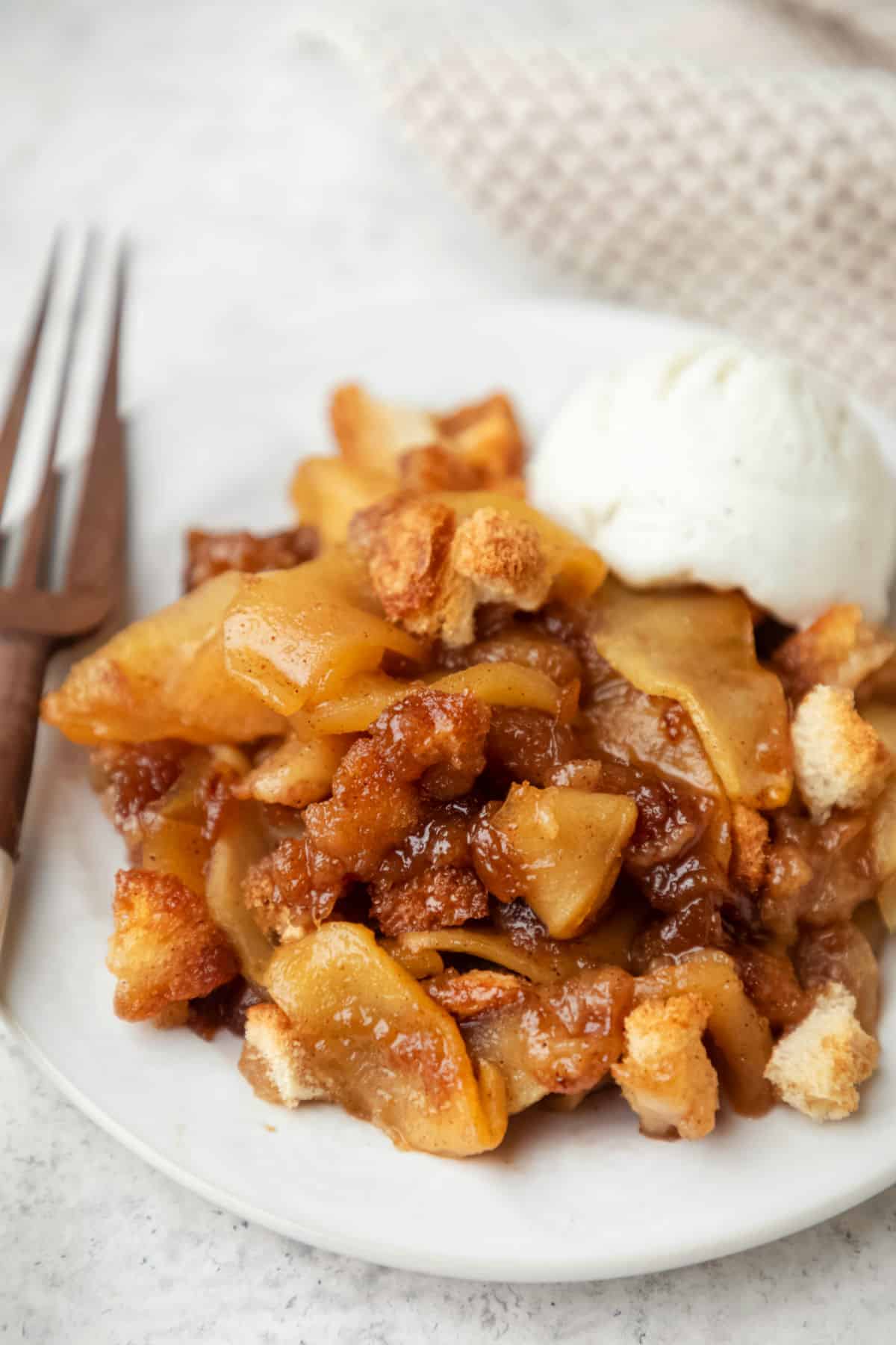 A white plate with apple brown betty and a scoop of vanilla ice cream.