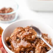 A dish of caramel apple cobbler cake next to a glass dish of pecans.