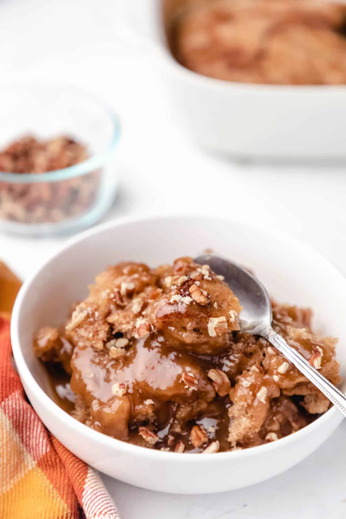 A dish of caramel apple cobbler cake next to a glass dish of pecans.