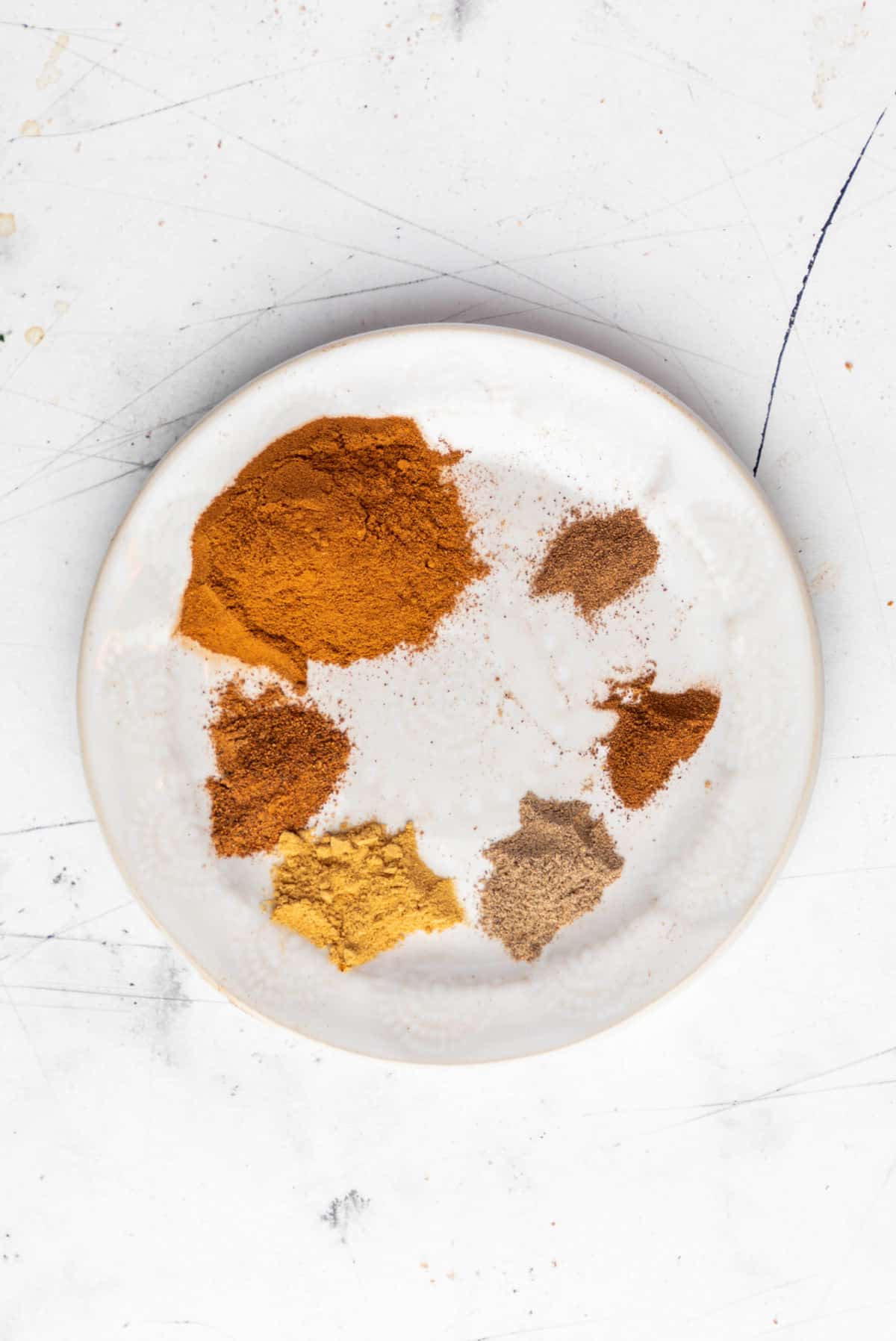 A white plate with spices for apple pie spice. 