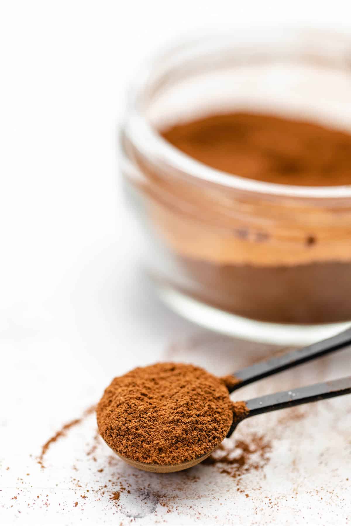 A black metal measuring spoon full of apple pie spice in front of the jar of spice. 