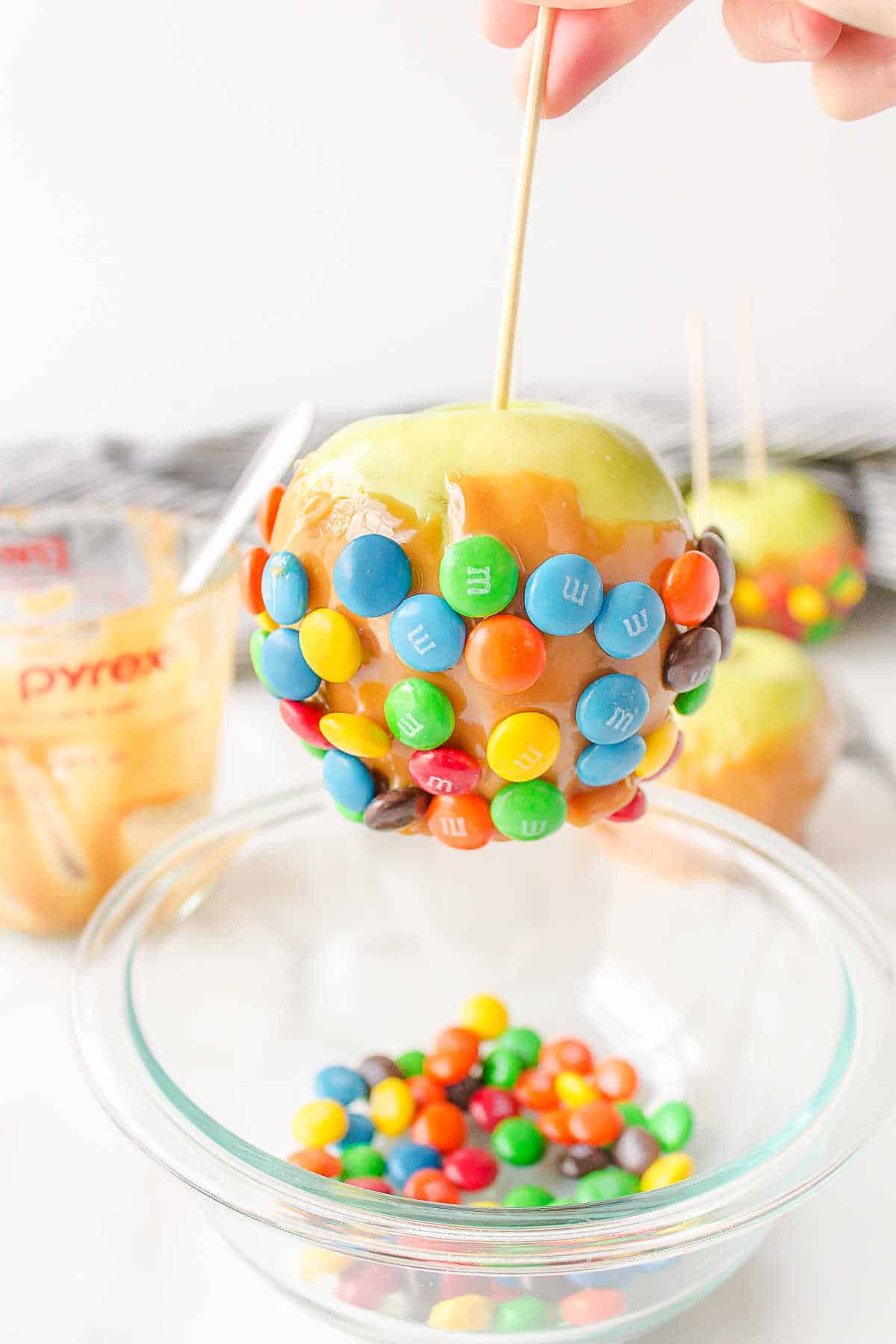 A caramel apple on a stick getting coated in M&Ms.