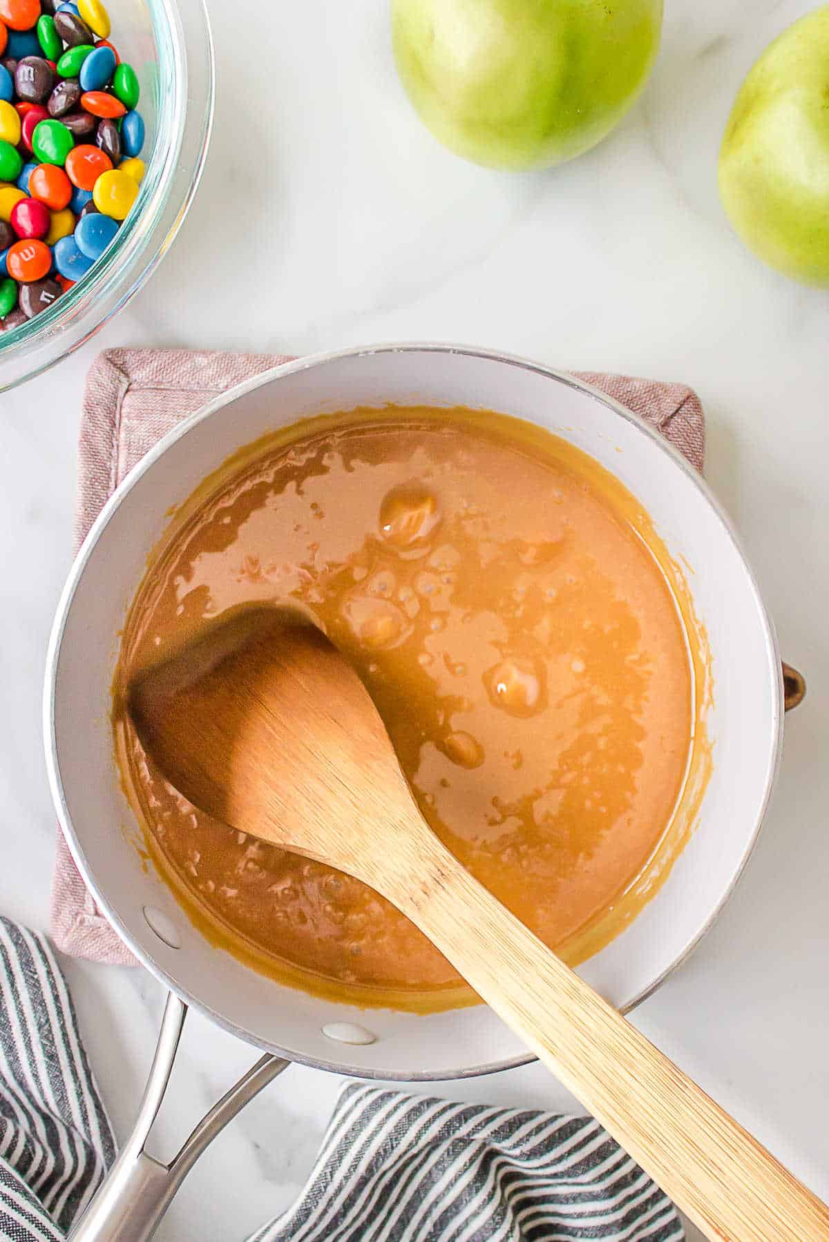 A wooden spoon stirring melted caramel in a saucepan. 
