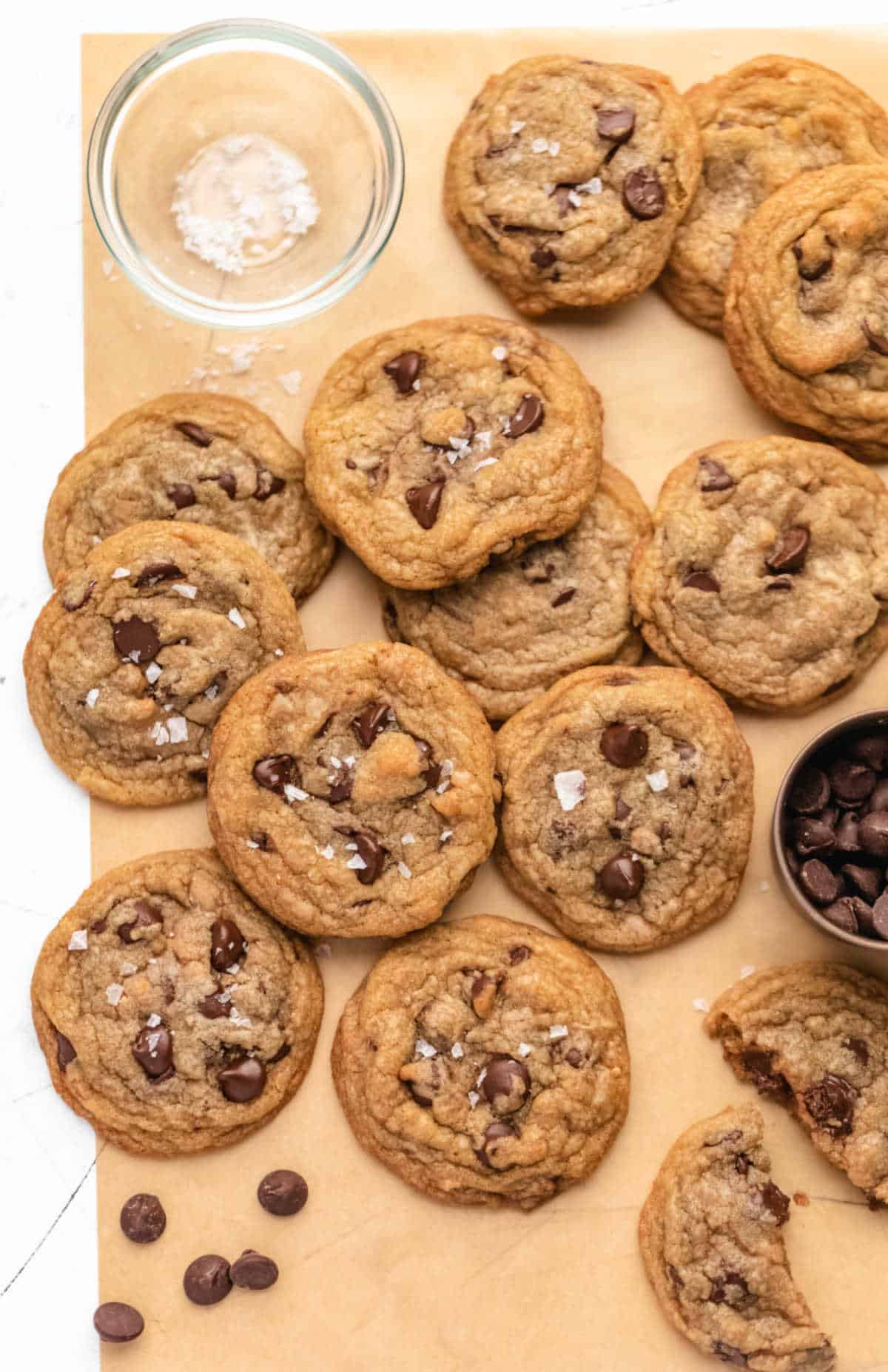 Toffee chocolate chip cookies next to dishes of salt and chocolate chips. 