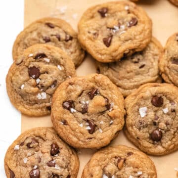 Toffee chocolate chip cookies in stacks on a piece of brown parchment paper.