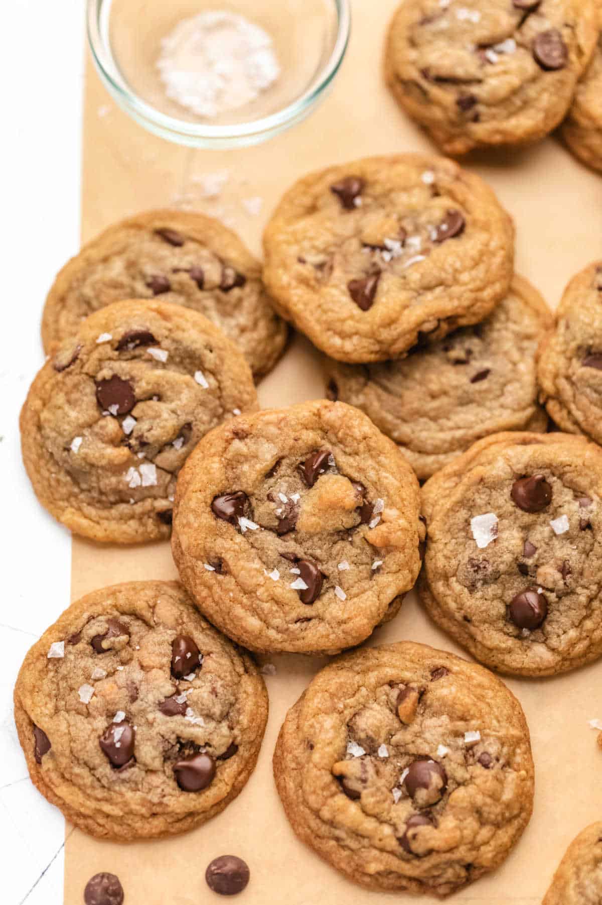 Toffee chocolate chip cookies in stacks on a piece of brown parchment paper.