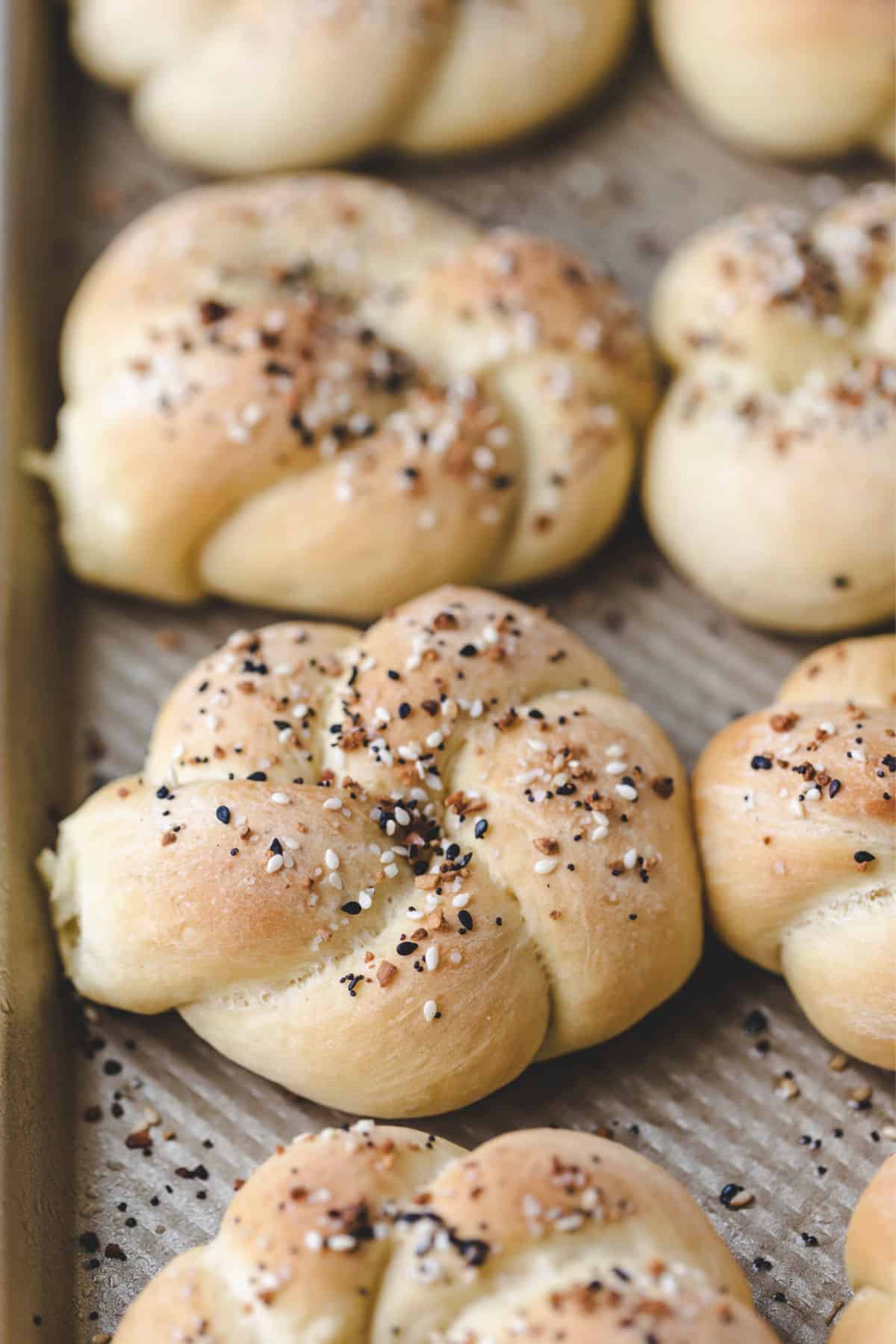 A row of everything bagel knots on a pan. 