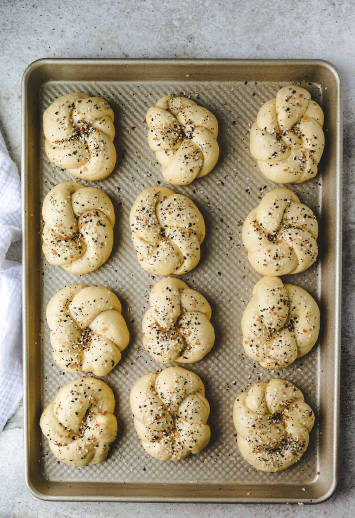 Unbaked everything bagel knots on a baking sheet. 