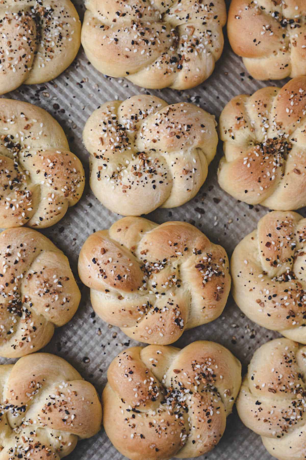 Three rows of everything bagel knots on a baking pan.