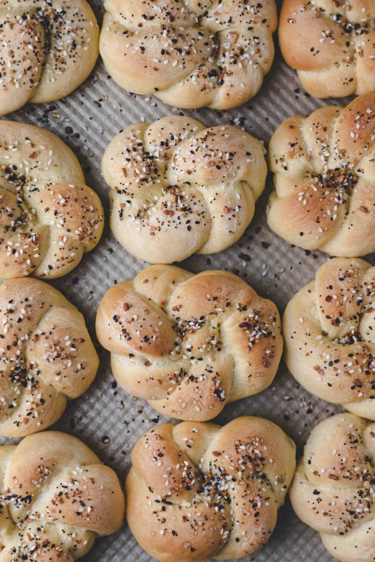 Three rows of everything bagel knots on a baking pan. 