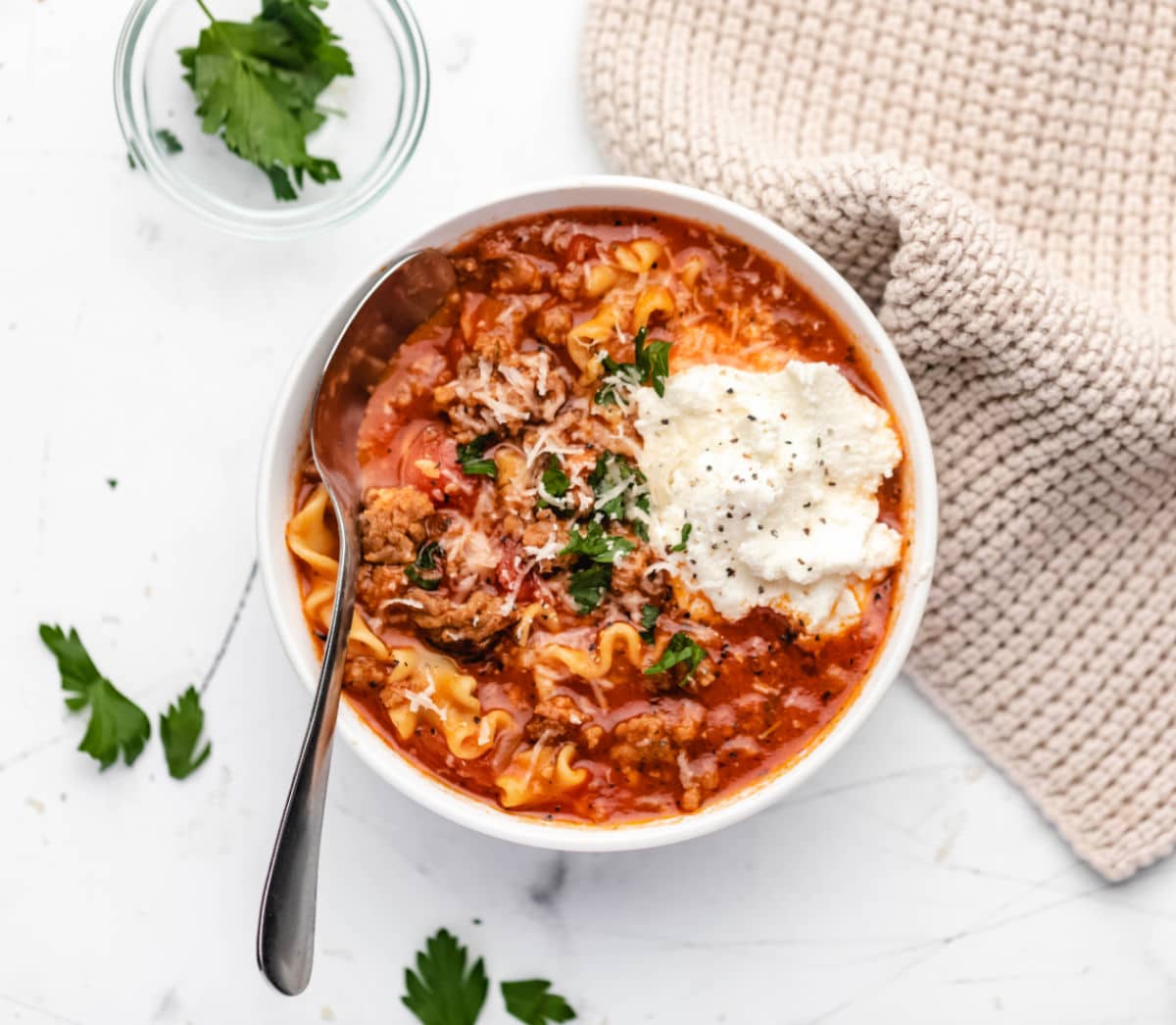 A bowl of lasagna soup next to a dish of parsley. 