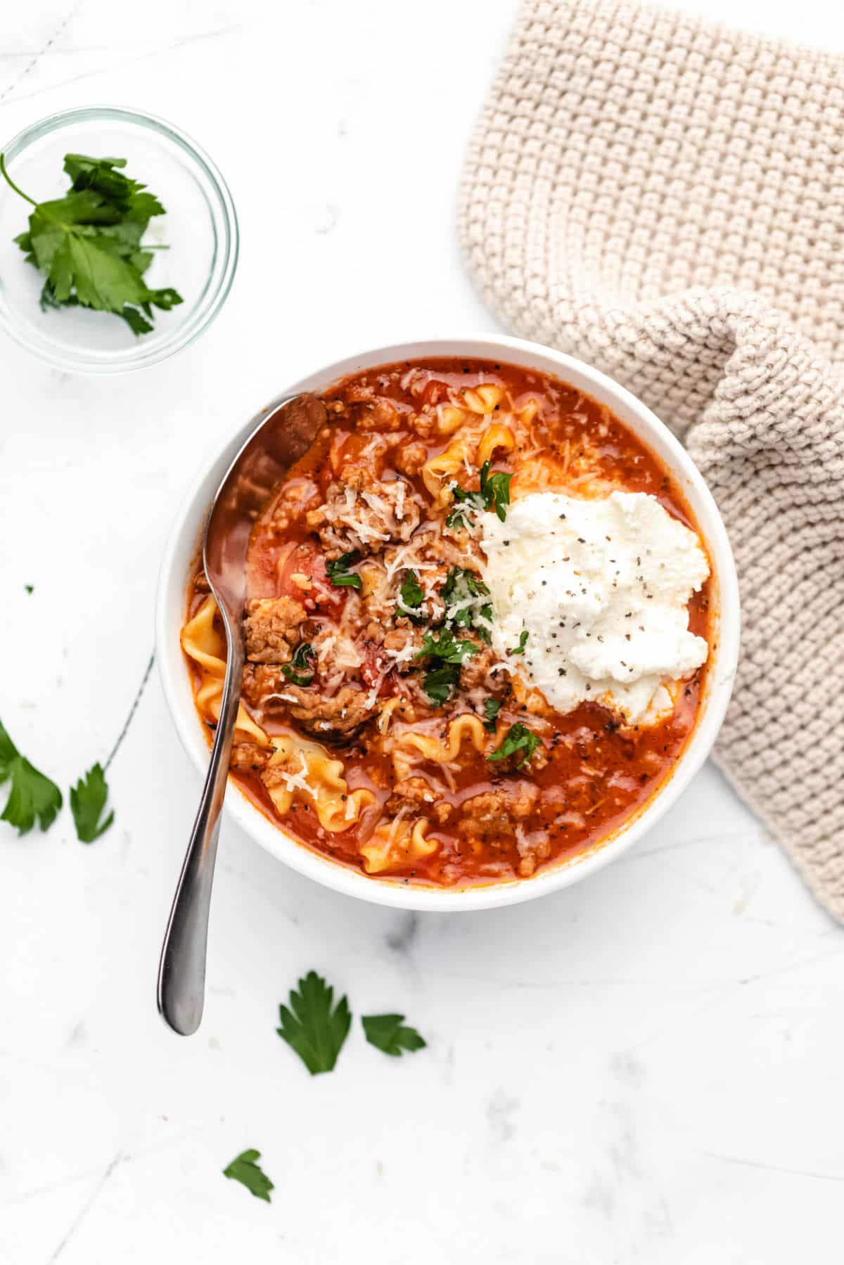 A bowl of lasagna soup next to a chunky knit napkin. 