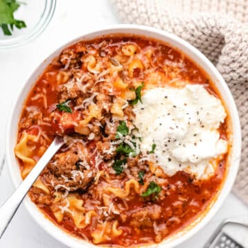 A bowl of lasagna soup topped with a scoop of ricotta cheese and parmesan cheese.