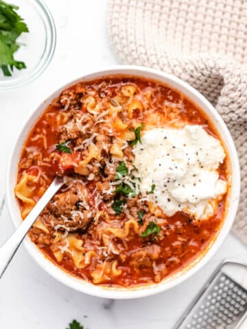 A bowl of lasagna soup topped with a scoop of ricotta cheese and parmesan cheese.