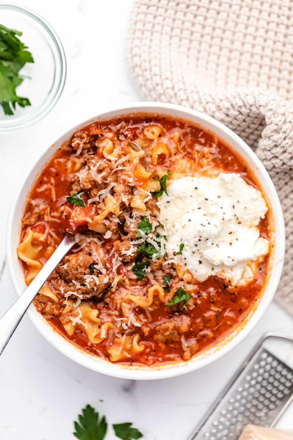 A bowl of lasagna soup topped with a scoop of ricotta cheese and parmesan cheese. 