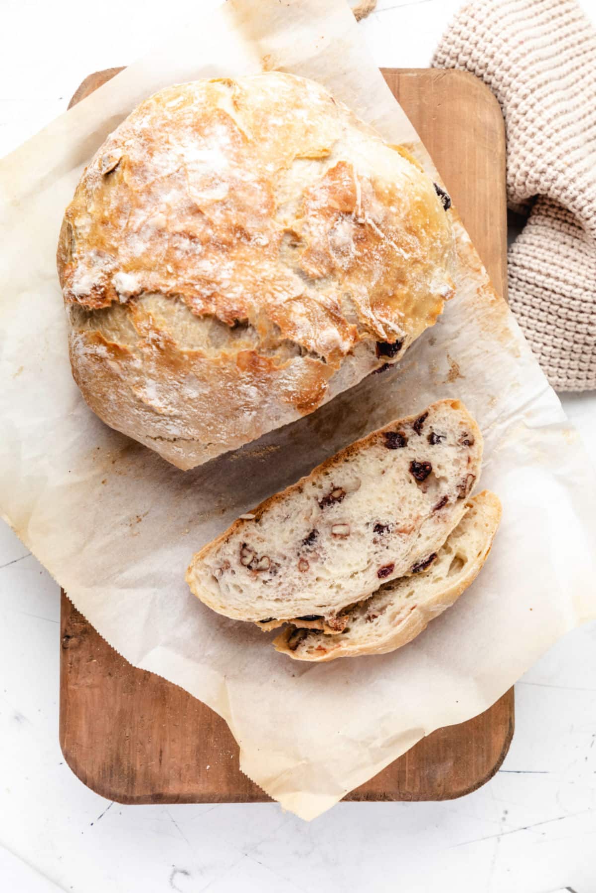 A loaf of no knead cranberry nut bread on a cutting board with two slices cut.  