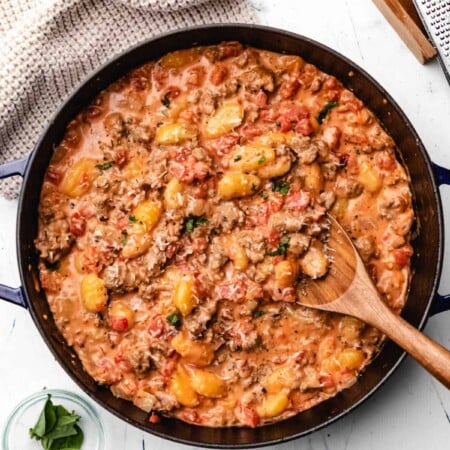 Pan of creamy sausage gnocchi with a wooden spoon in it.