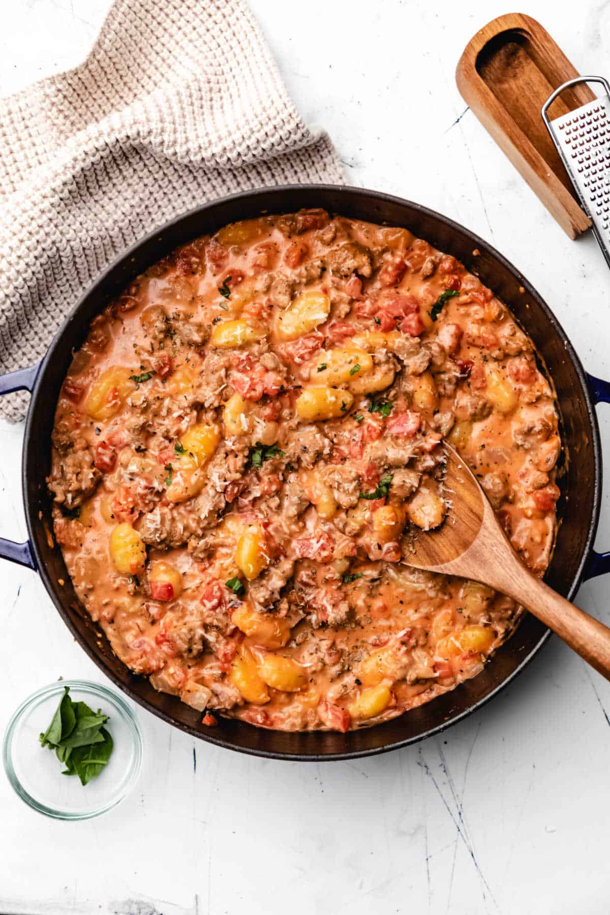 Pan of creamy sausage gnocchi with a wooden spoon in it.