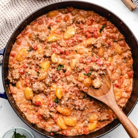 A wooden spoon scooping up gnocchi in sauce.