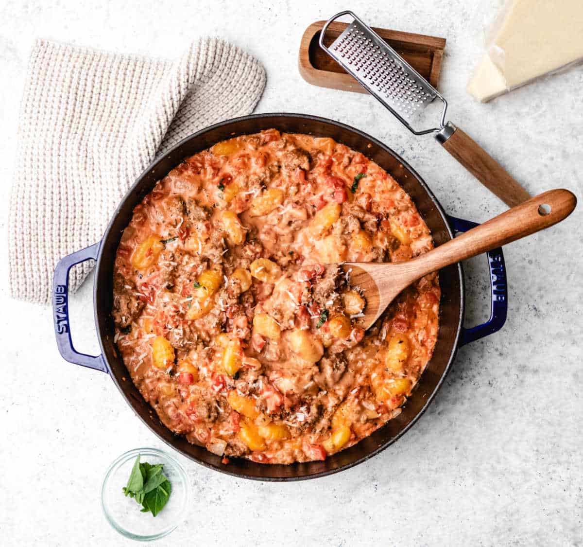 A pot of sausage gnocchi next to a cheese grater and a block of parmesan cheese. 