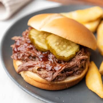 A slow cooker barbecue beef sandwich next to fries on a plate.