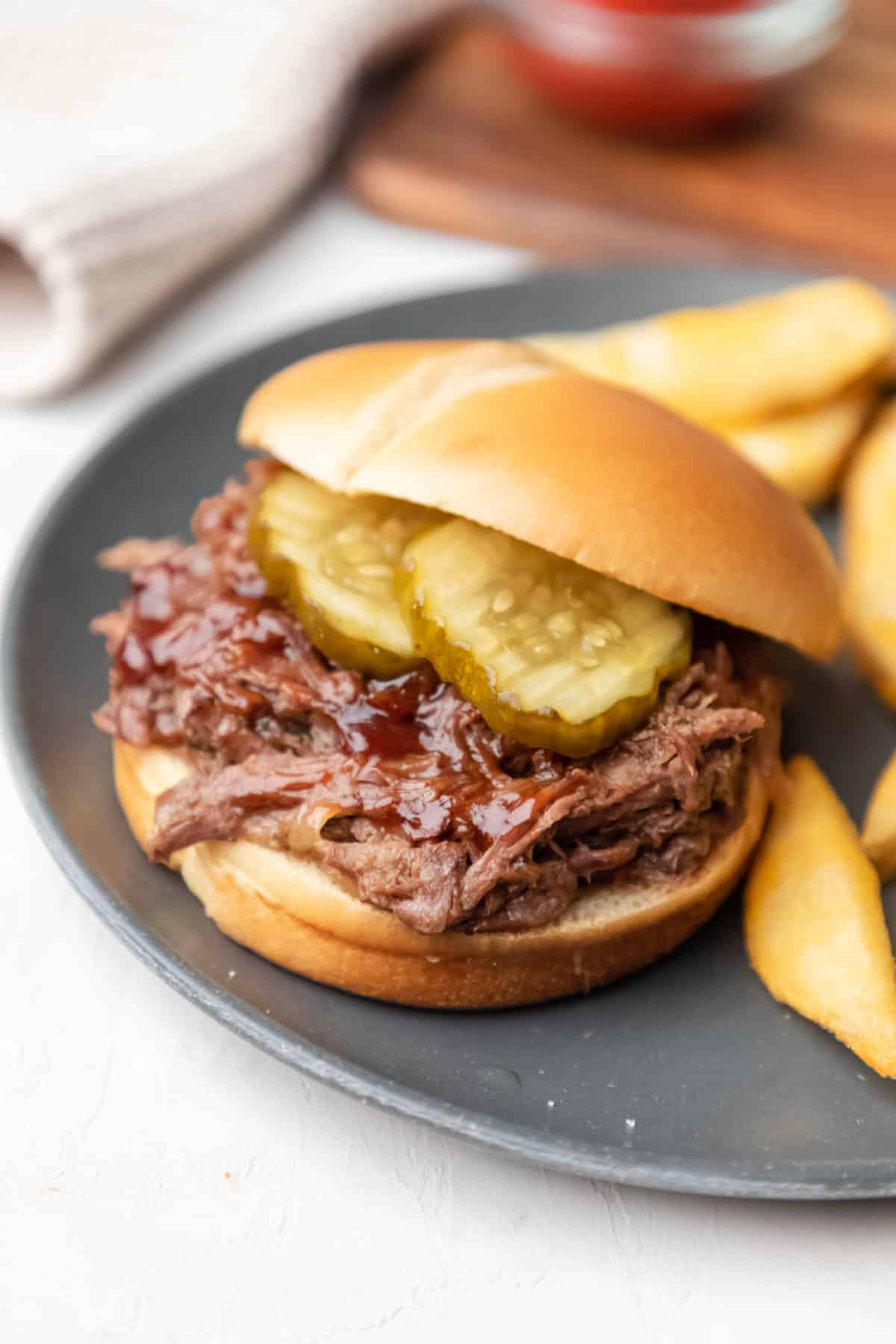 A slow cooker barbecue beef sandwich next to fries on a plate.