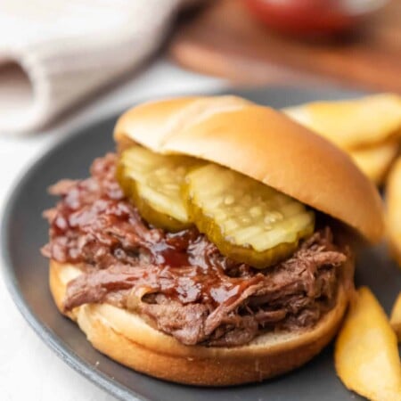 Slow cooker barbecue beef on a bun topped with pickles.