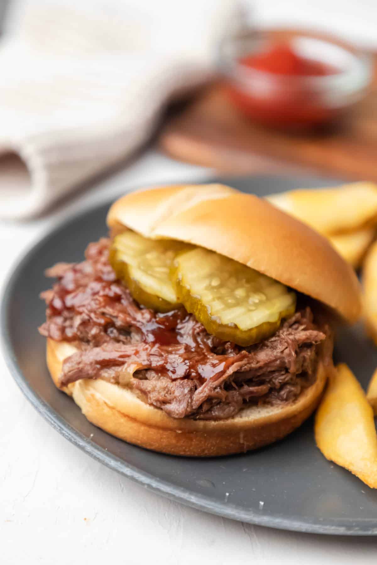 Slow cooker barbecue beef sandwich and fries on a gray plate. 