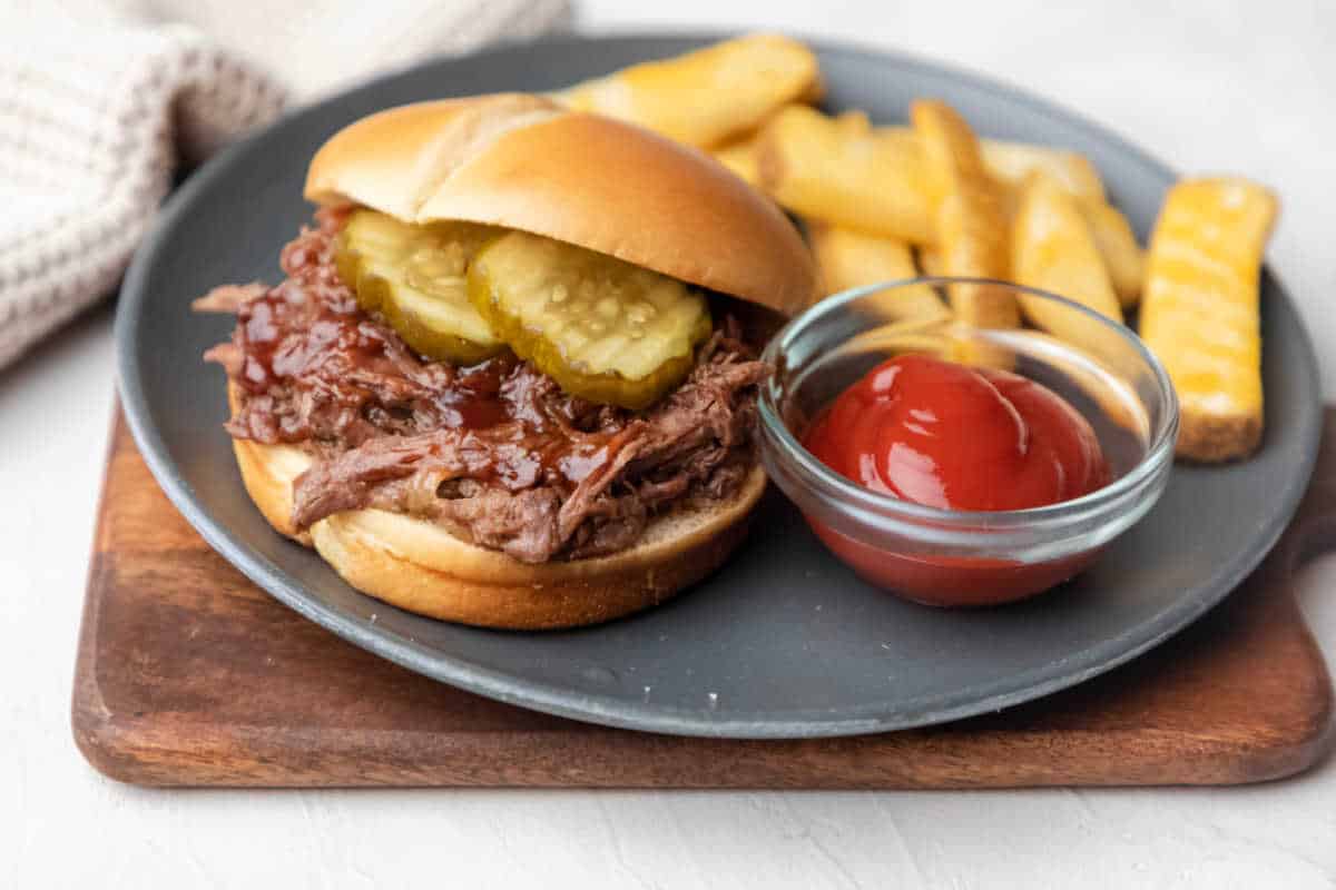 A barbecue beef sandwich next to a dish of ketchup and fries.